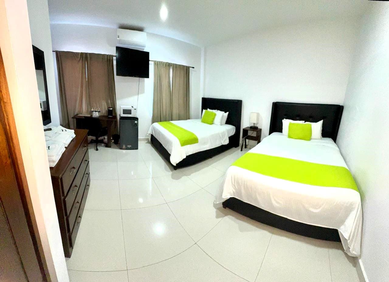 A modern hotel room featuring two beds with green accents, a desk, and a television.