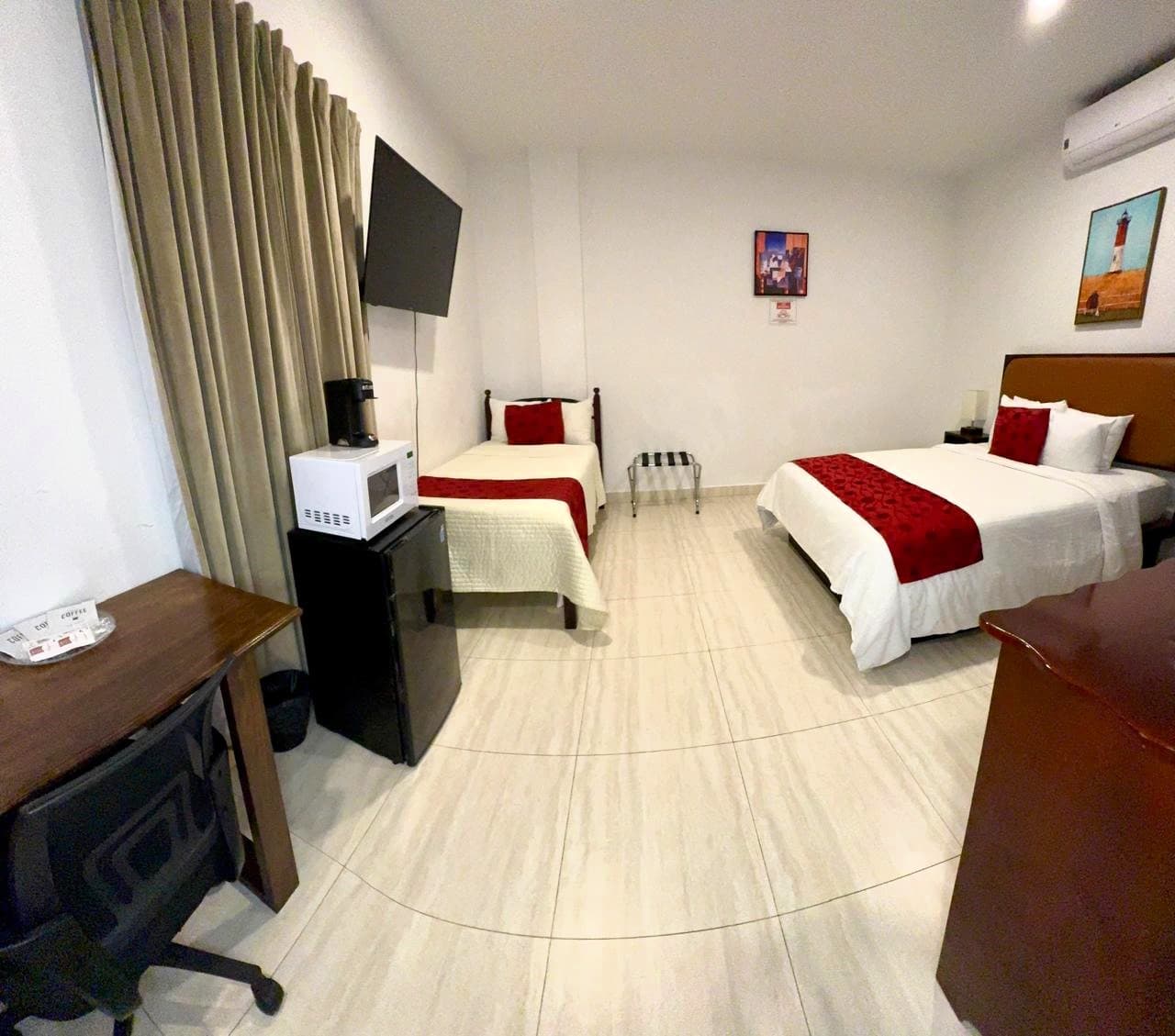 A hotel room featuring two beds, a desk, a TV, and a mini-fridge.