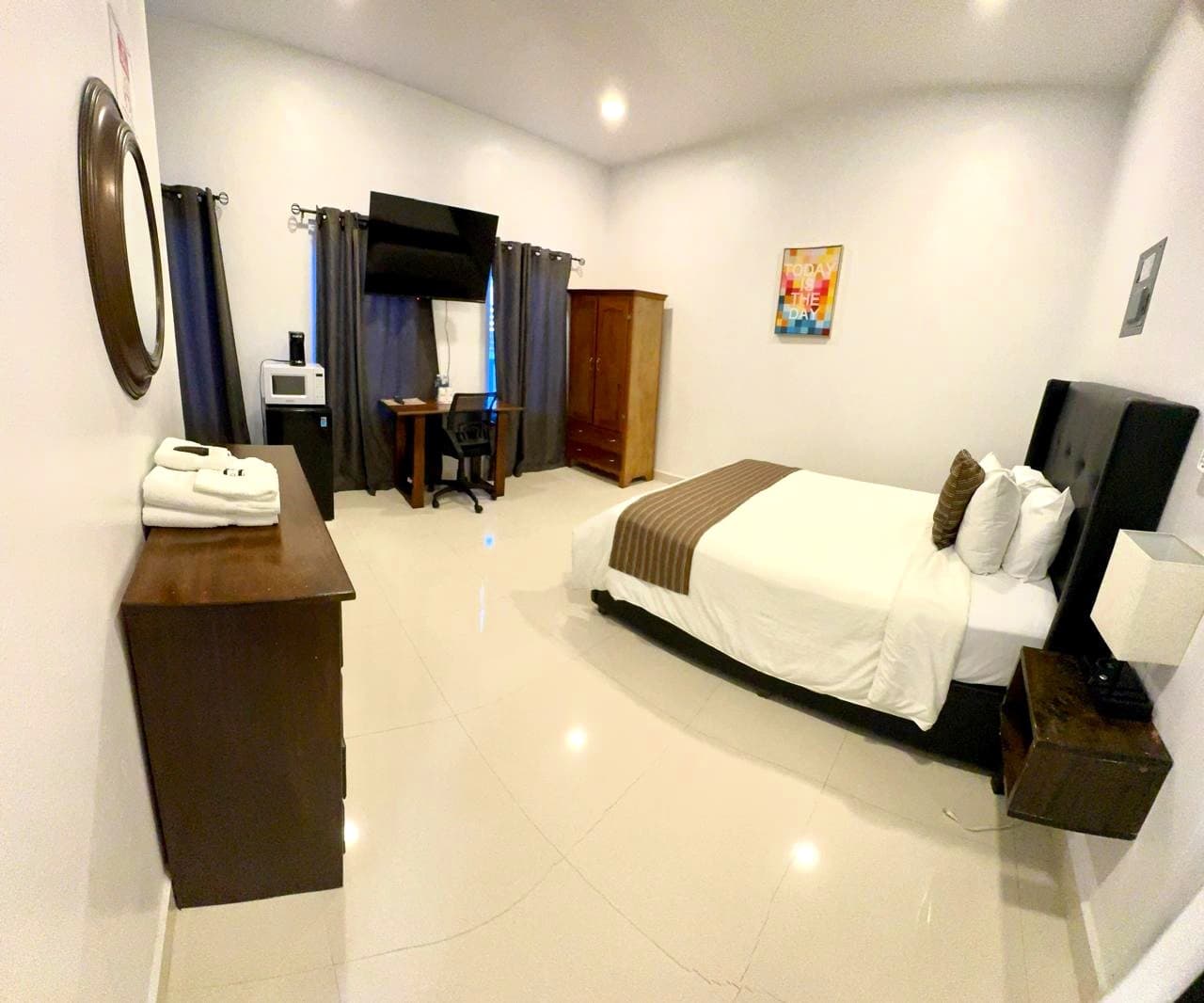 A spacious guest room featuring a bed, desk, microwave, TV, and dark curtains.