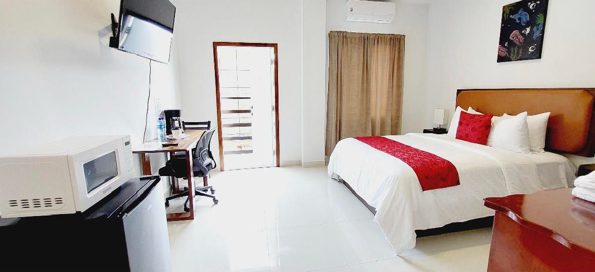 Bedroom with refrigerator and microwave in the foreground and bright white floors.